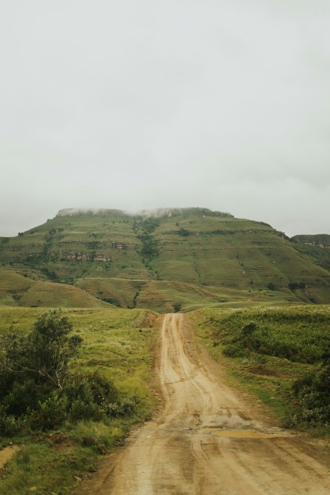 a dirt road with a hill in the background Zsu