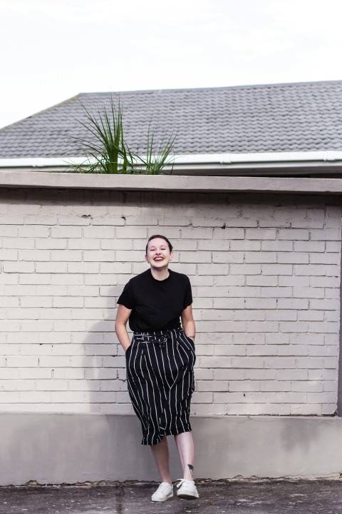 woman in black scoop neck shirt and black and white skirt standing beside gray wall