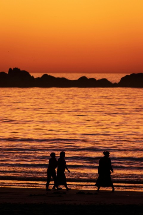 a group of people walking along a beach at sunset