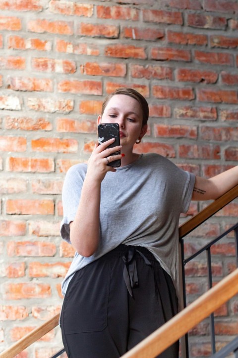 woman in gray crew neck t shirt and black skirt holding black smartphone