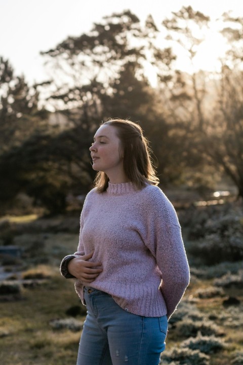 woman in white sweater and blue denim jeans standing near trees during daytime