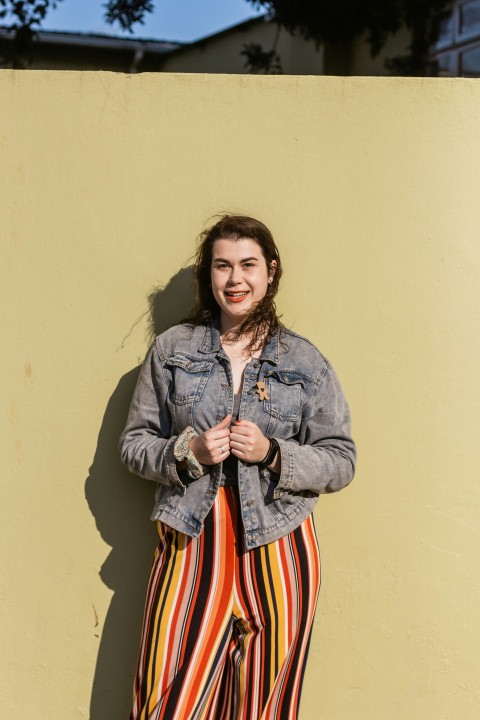 woman in gray jacket standing beside yellow painted wall