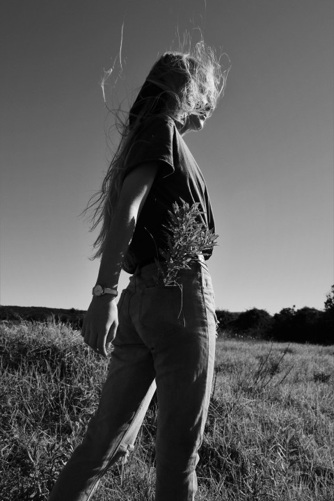 grayscale photo of woman in black tank top and pants standing on grass field E