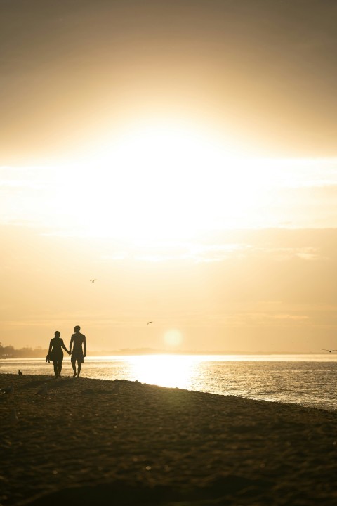 two people walking on a beach at sunset