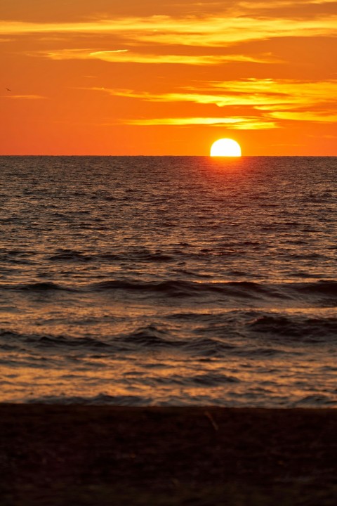 the sun is setting over the ocean on a cloudy day