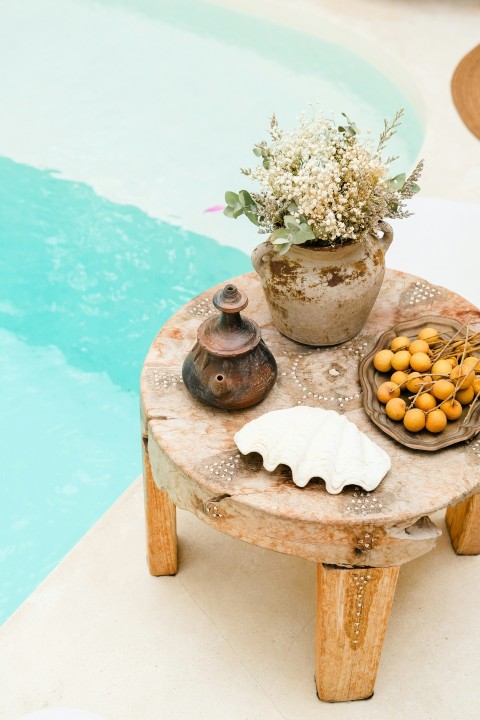 a wooden table with a potted plant on it next to a pool