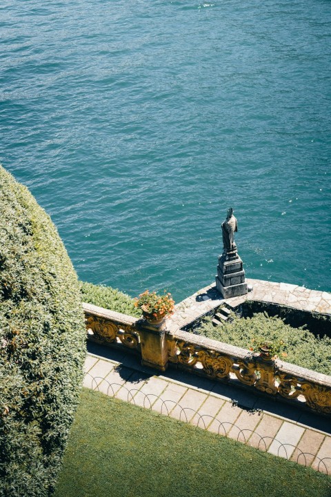 a statue sitting on top of a lush green hillside next to a body of water