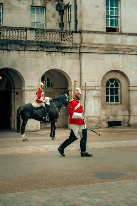 a man in uniform walking a horse in front of a building