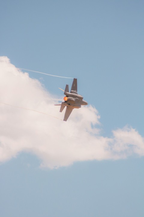 a fighter jet flying through a cloudy blue sky