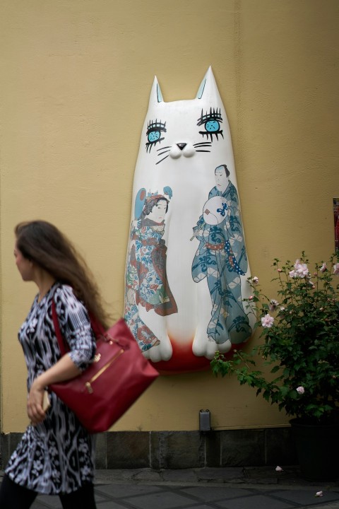 a woman walking down a street past a statue of a cat