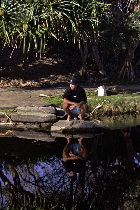 a man sitting on a rock next to a body of water