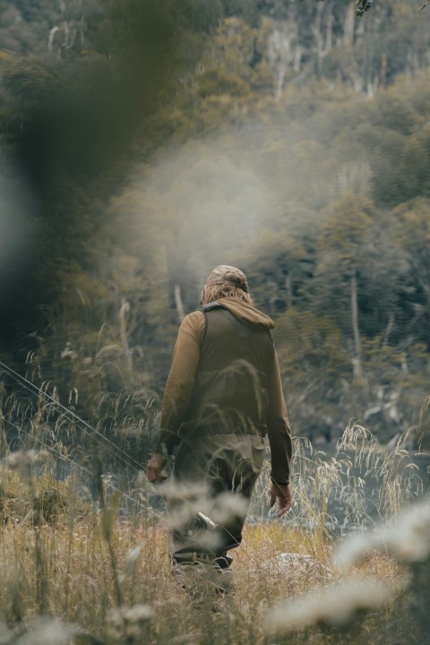 a man walking through tall grass with a fishing pole