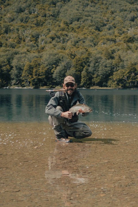 a man kneeling in the water holding a fish