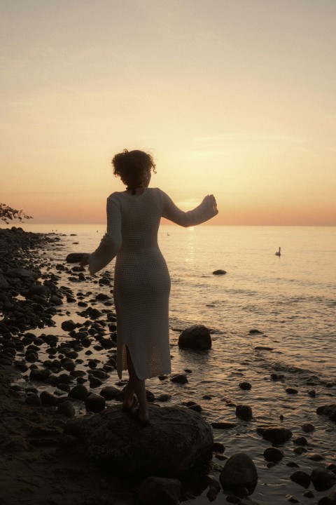 a woman standing on a rocky beach at sunset MWGP4Dkee