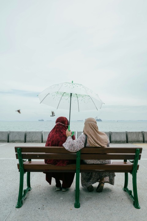 a couple of women sit on a bench under an umbrella 6d