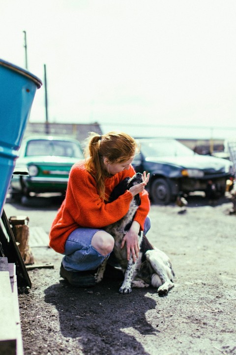 a woman in an orange sweater petting a dog