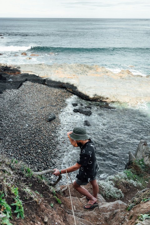 man in black jacket and orange cap standing on rocky shore during daytime