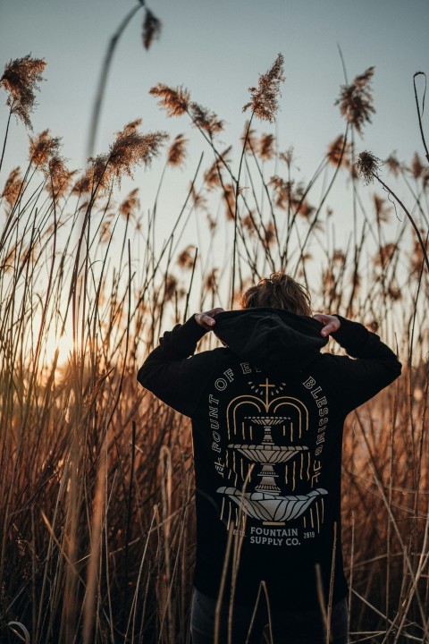 woman in black and yellow hoodie standing on brown grass field during daytime