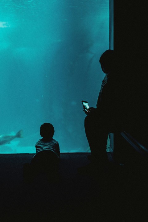 two people looking at a cell phone in front of a large aquarium