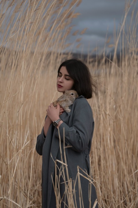 a woman standing in a field holding a teddy bear