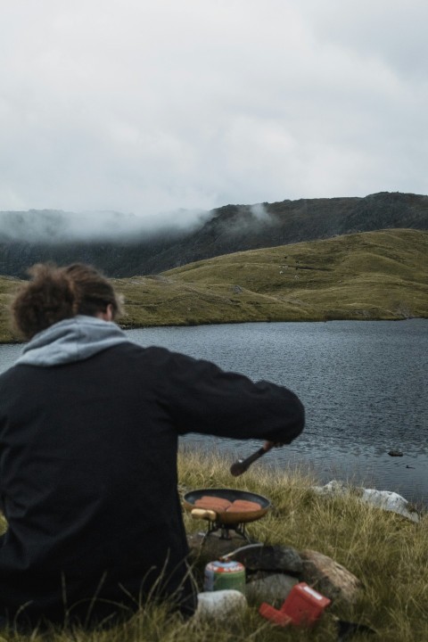 person in black hoodie standing on green grass field near body of water during daytime