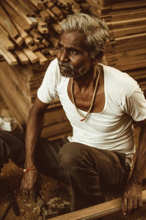 man in white crew neck t shirt and brown pants sitting on brown wooden chair