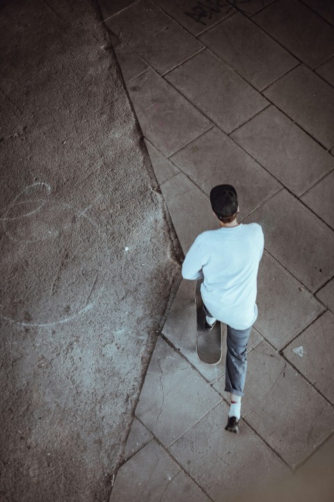 man wearing white shirt and black cap while riding on skateboard