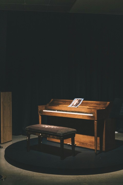 brown wooden upright piano with ottoman bench and light turned on lk