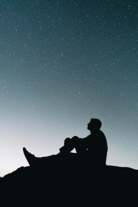 a man sitting on top of a hill under a night sky