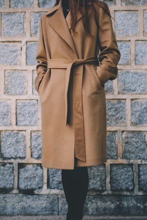 woman wearing brown single breasted coat standing in front of gray brick wall