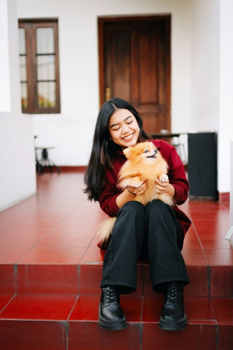 woman in red long sleeve shirt holding brown long coated small dog