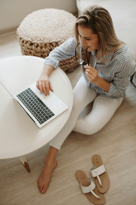 woman in white and black striped dress shirt sitting on floor in front of table while using laptop computer LO3IuL