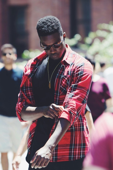 man fixing his red black and white plaid sport shirt sleeve during daytime