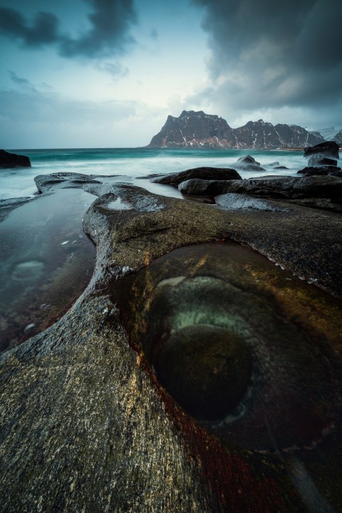 a large rock sitting on top of a beach under a cloudy sky