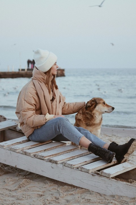 woman in brown jacket and blue denim jeans sitting on brown wooden bench during daytime Dz