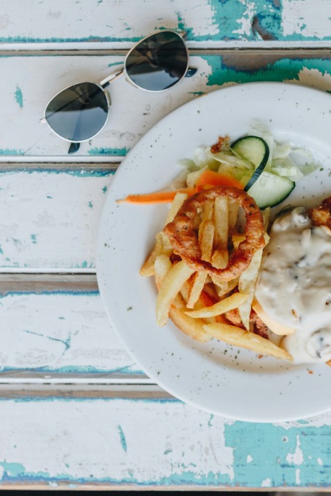 potato fries with sliced cucumber and sauce on a round plate near silver framed aviator style sunglasses