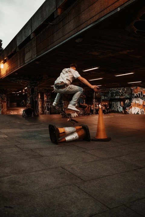 man in white t shirt and blue denim jeans sitting on orange and black skateboard during