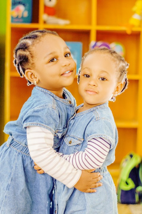 two young girls hugging each other in front of a bookshelf URFQo8s