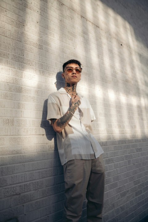 a man leaning against a brick wall wearing sunglasses