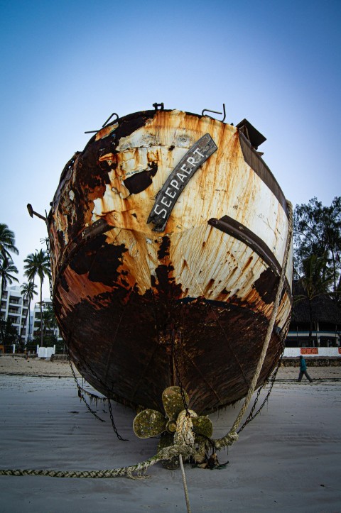 a rusted boat sitting on top of a sandy beach