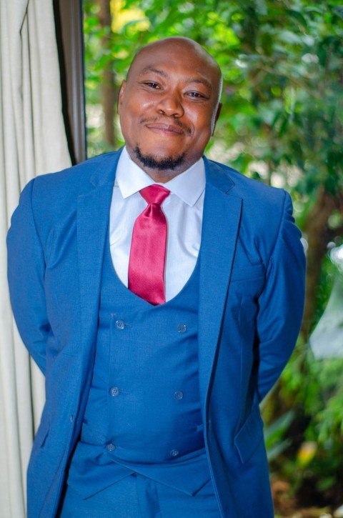 man in blue suit jacket standing near green trees during daytime