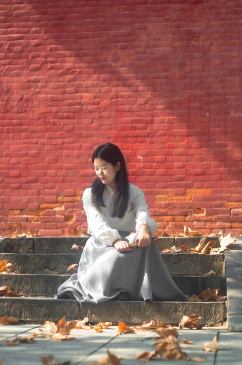 woman sitting on gray stair near leaves during daytime