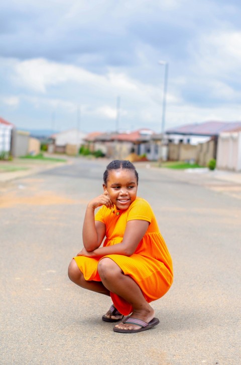 boy in yellow t shirt and orange shorts sitting on gray concrete floor during daytime