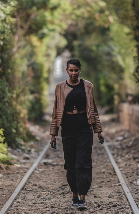 a woman walking down a train track with trees in the background