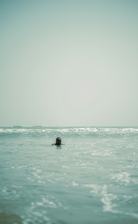 a person swimming in the ocean with a boat in the background