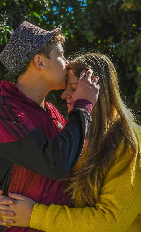 woman in red long sleeve shirt kissing woman in black and white knit cap TJRO03siO