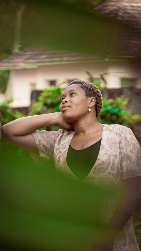 a woman leaning against a tree with a house in the background