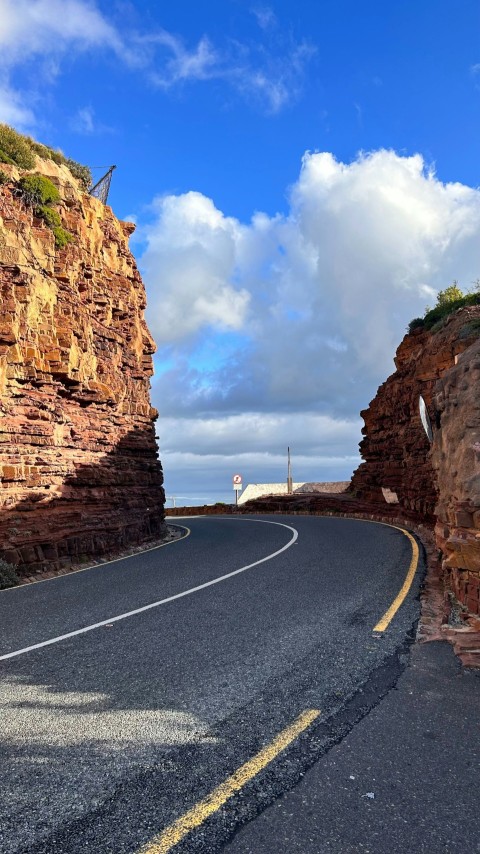 a curved road with a rock cliff in the background