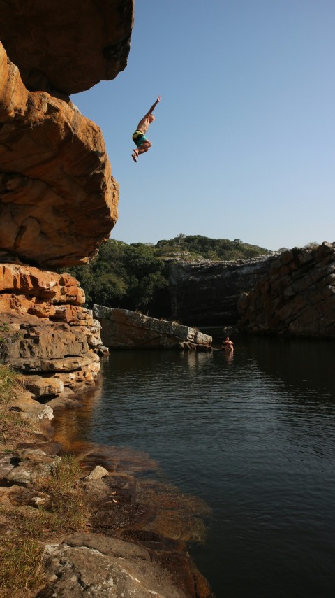 man jumping off rocky mountain above body of water dFJgwzB