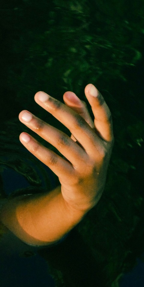 a persons hand reaching for a frisbee in the water